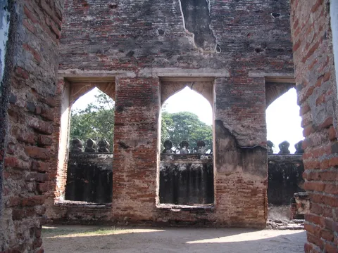 A ruined brick wall with three pointed arched windows and trees beyond