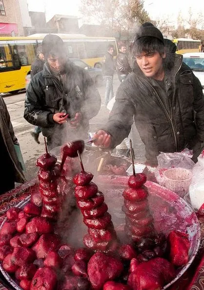 Vendors behind skewers of red food beside a steaming pot