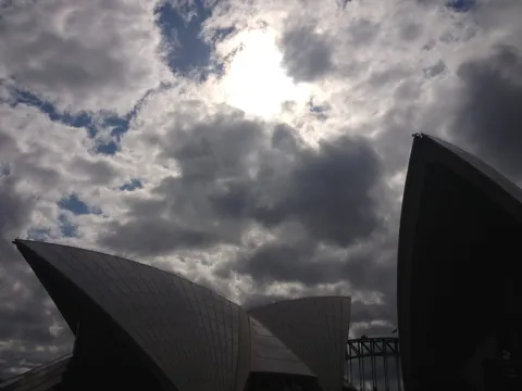 Silhouetted sail-shaped roofs beneath a dramatic cloudy sky