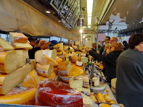 People shopping at a market stall piled with cheeses