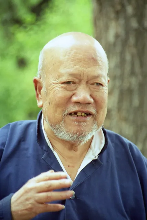 An older man with a white beard holding a cigarette outdoors