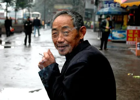 An older man smoking a cigarette on a busy street