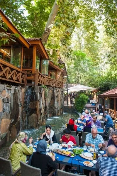 People eating at tables beside a tree-lined stream