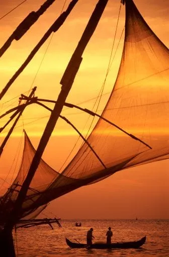 Silhouettes of fishing nets and a small boat against an orange sunset