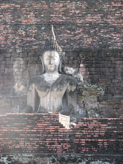 A seated Buddha statue against a weathered brick temple wall