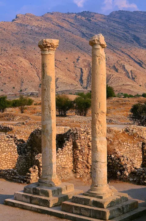 Two tall stone columns above crumbling walls with dry mountains behind