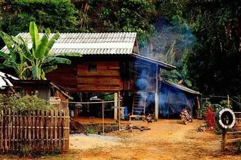 A raised wooden house behind a fence, with smoke drifting nearby