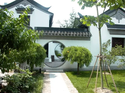 A garden with circular doorways in white walls and trimmed shrubs