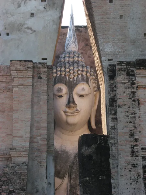 A seated Buddha statue seen through a tall slit in a brick wall